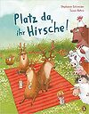 Drei Hirsche sitzen auf einer rot/orangenen Decke auf einer Wiese und werden von anderen Tieren beobachtet