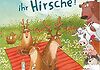 Drei Hirsche sitzen auf einer rot/orangenen Decke auf einer Wiese und werden von anderen Tieren beobachtet
