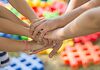 Übereinandergelegte Kinderhände vor farbigen Hintergrund